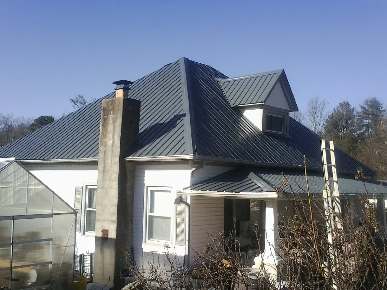 Dark blue standing seam metal roof on a white farmhouse with dormer — Slate & Tile Roof Repair by Roofing Brothers in Ellston