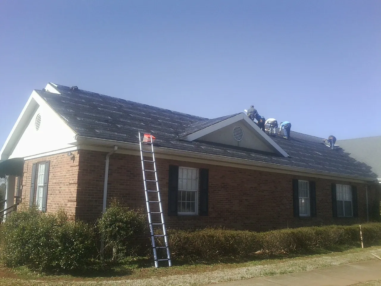 Crew tearing shingles off a brick ranch roof with a ladder set — Metal Roof Repair work by our crew in Ellston