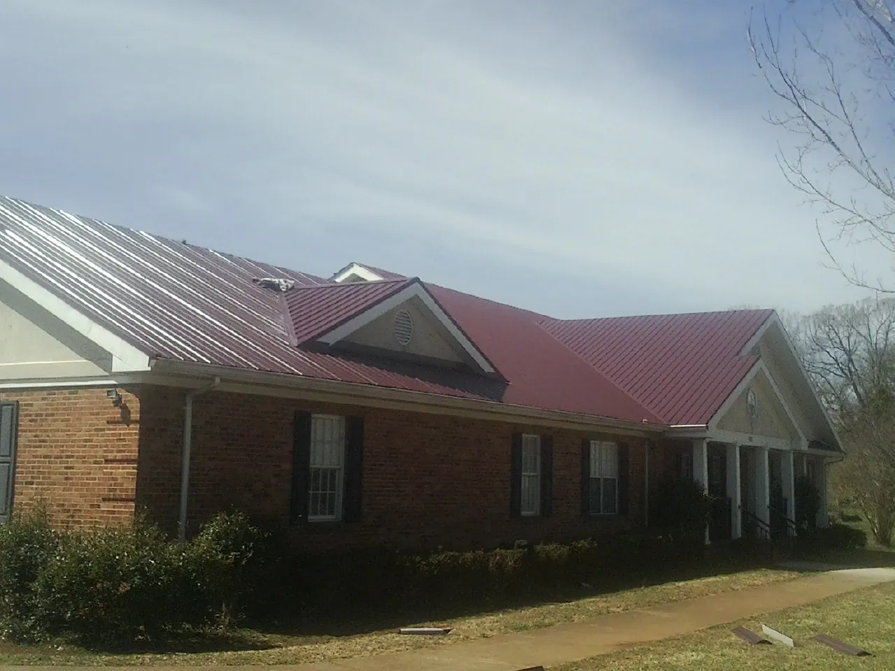 Red metal roof with gabled entries on a long brick building, from a Hail Damage Roof Repair job in Ellston