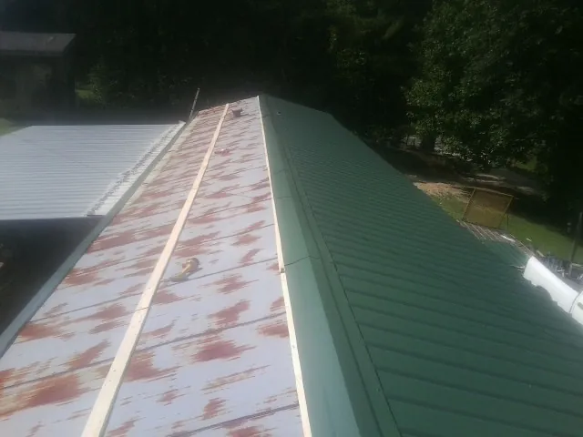 Old rusted panels beside newly installed green metal roofing — Wind Damage Roof Repair by Roofing Brothers in Ellston