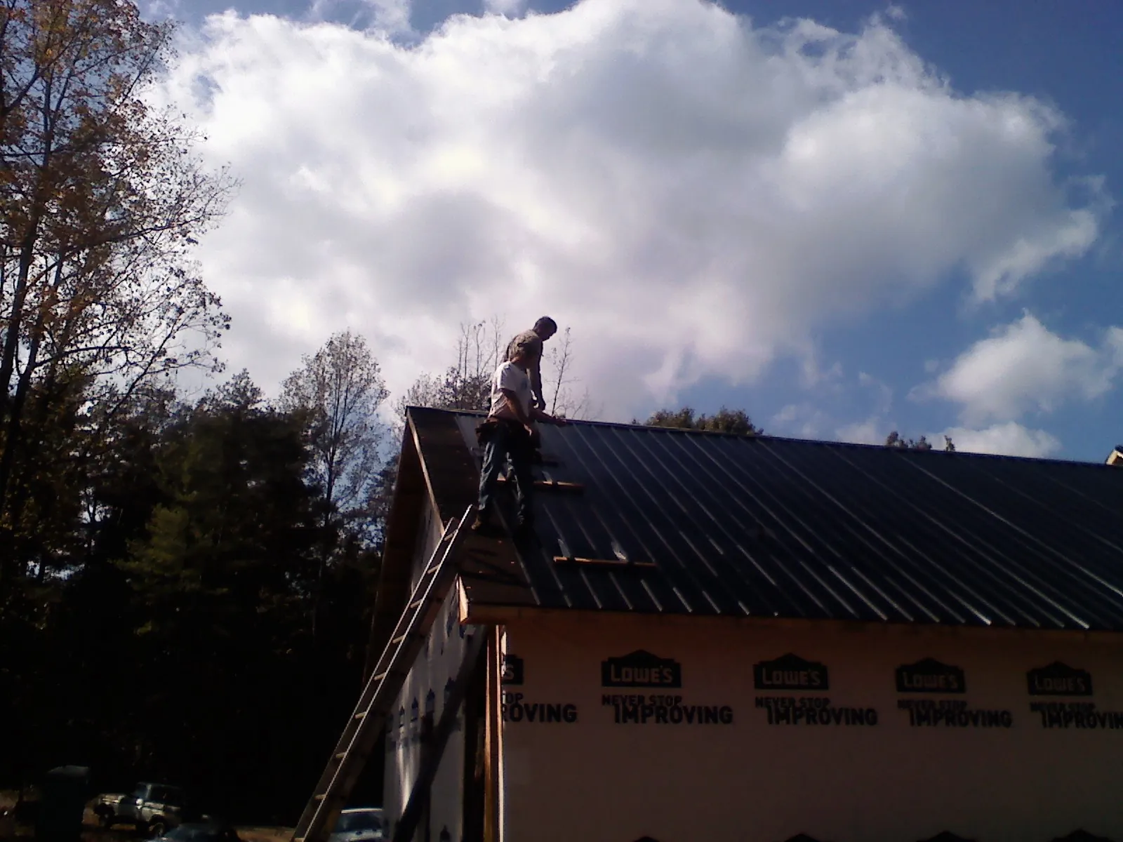 Roofer fastening dark metal panels high against a cloudy sky, from a Roof Inspection job in Ellston