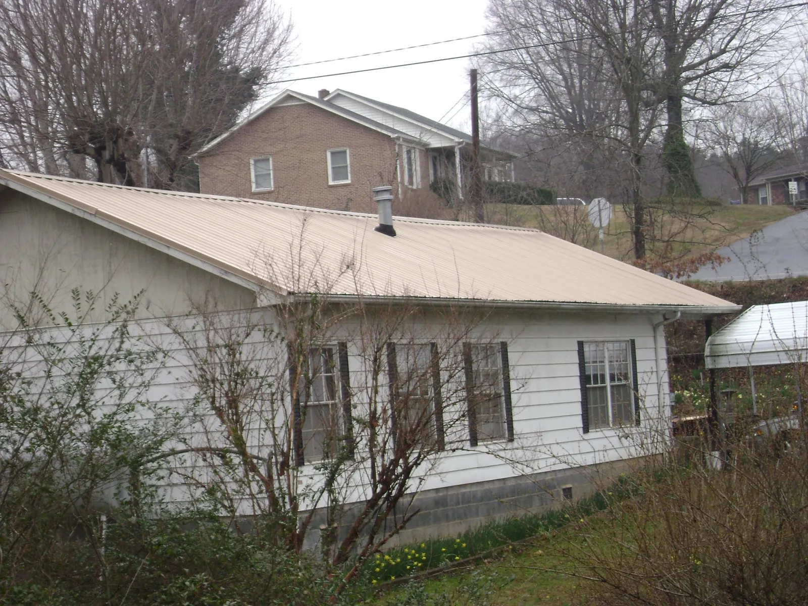 Tan metal roof on a white sided house set into a hillside — Commercial Roofing by Roofing Brothers in Ellston