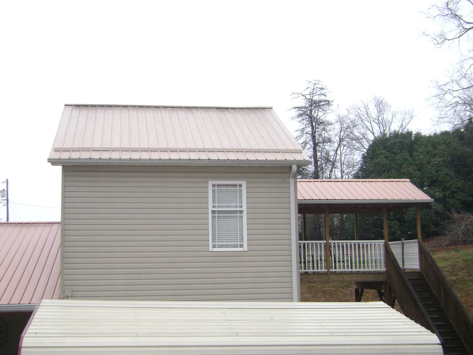Tan metal roofs on a two story addition and attached porch, from a Roof Replacement job in Ellston